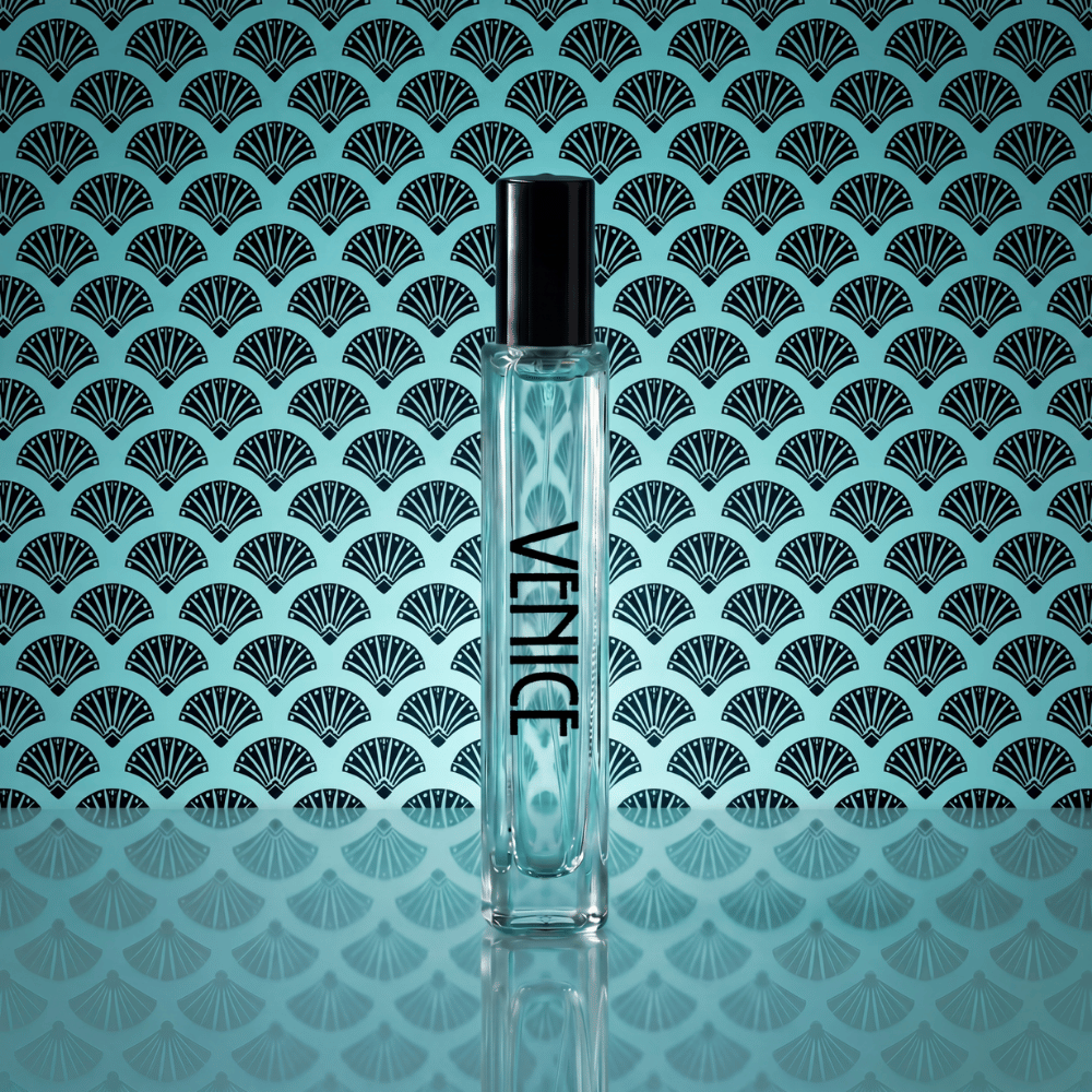 A clear cylindrical perfume bottle with a black cap stands centered against a turquoise background with a repeating black fan pattern. The bottle has the brand name 'VENICE' printed vertically in black.