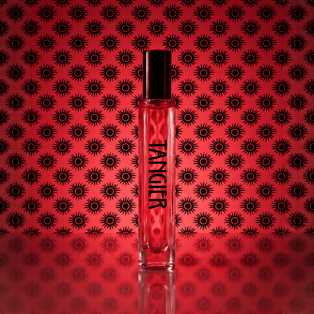 A clear rectangular perfume bottle with a black cap stands centered against a red background patterned with repeating black sunburst motifs. The bottle is labeled 'TANKIER' in black text.