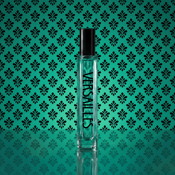A clear glass Versaces perfume bottle with a black cap, standing upright against a teal background with a repeating black damask pattern.